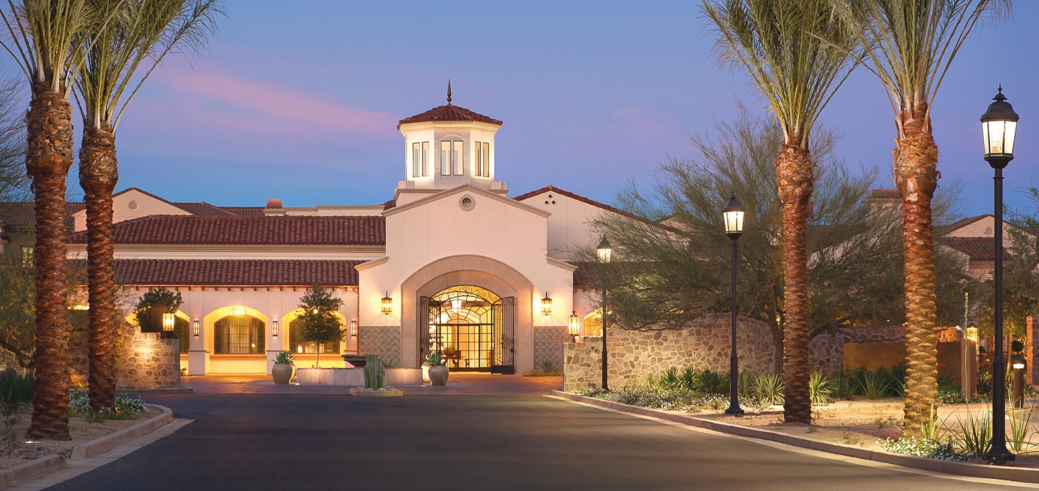 The community entrance at dusk adorned with palm trees creates a serene and inviting ambiance 