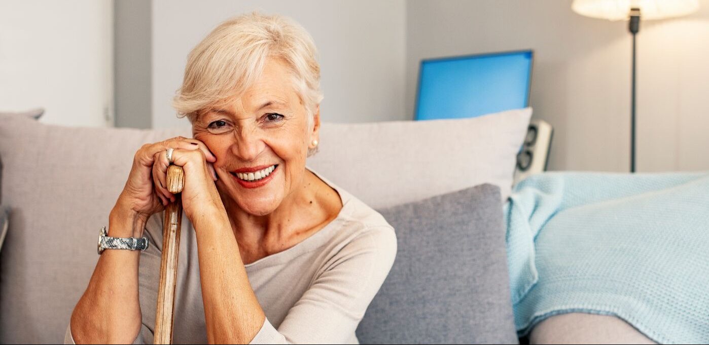 A contented elderly lady sits on a sofa, wearing a warm smile.