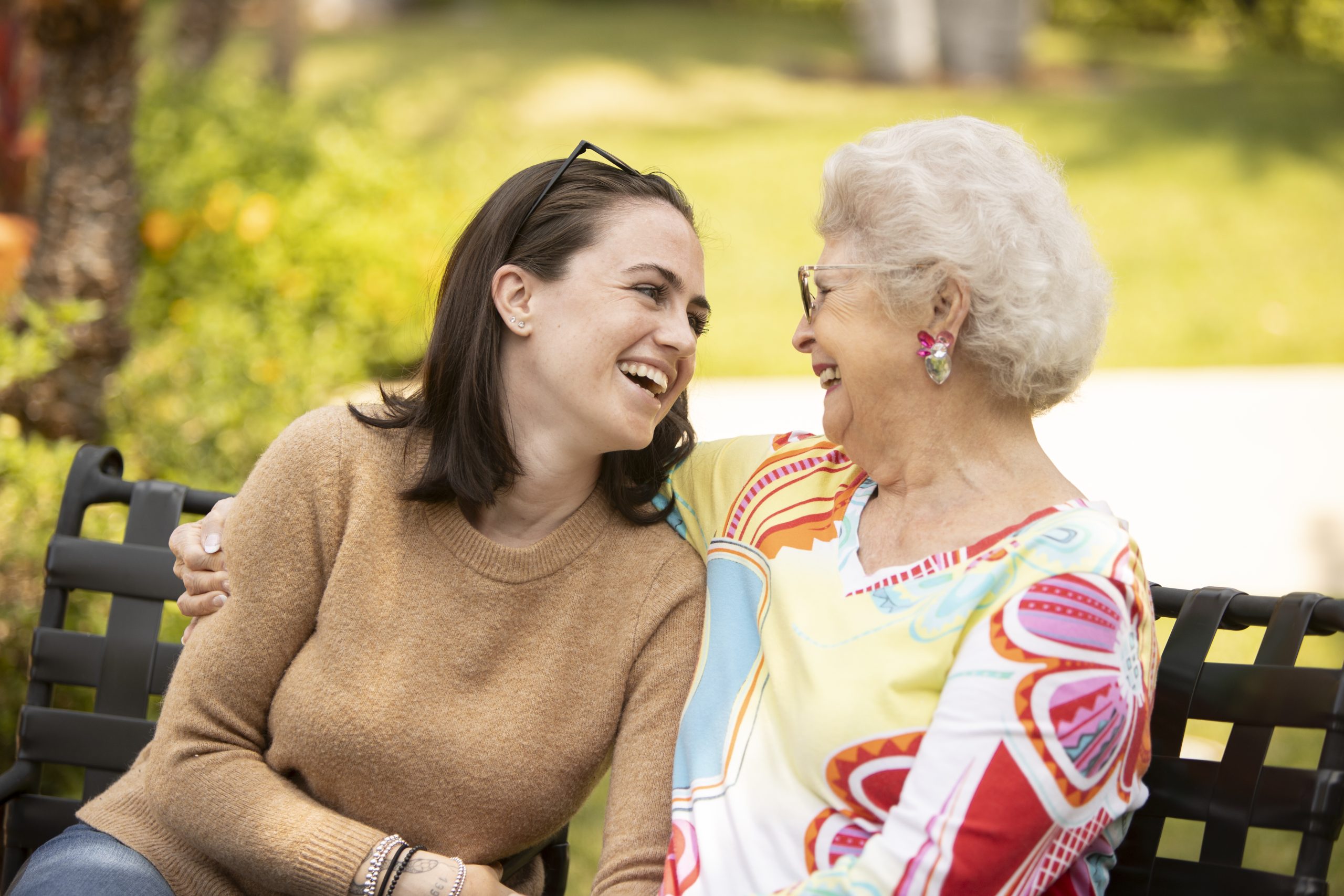 laughing elderly woman and her granddaughter while sitting on a bench