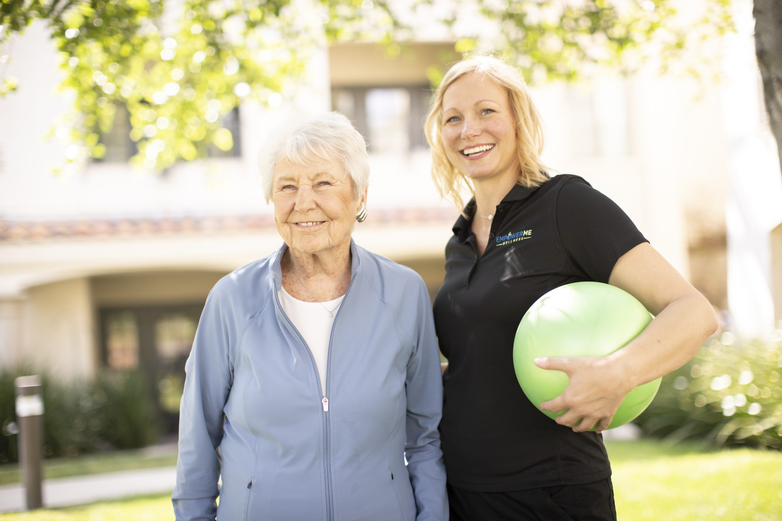 An exercise trainer and an older woman holding an exercise ball, showcasing a bond from a shared activity.