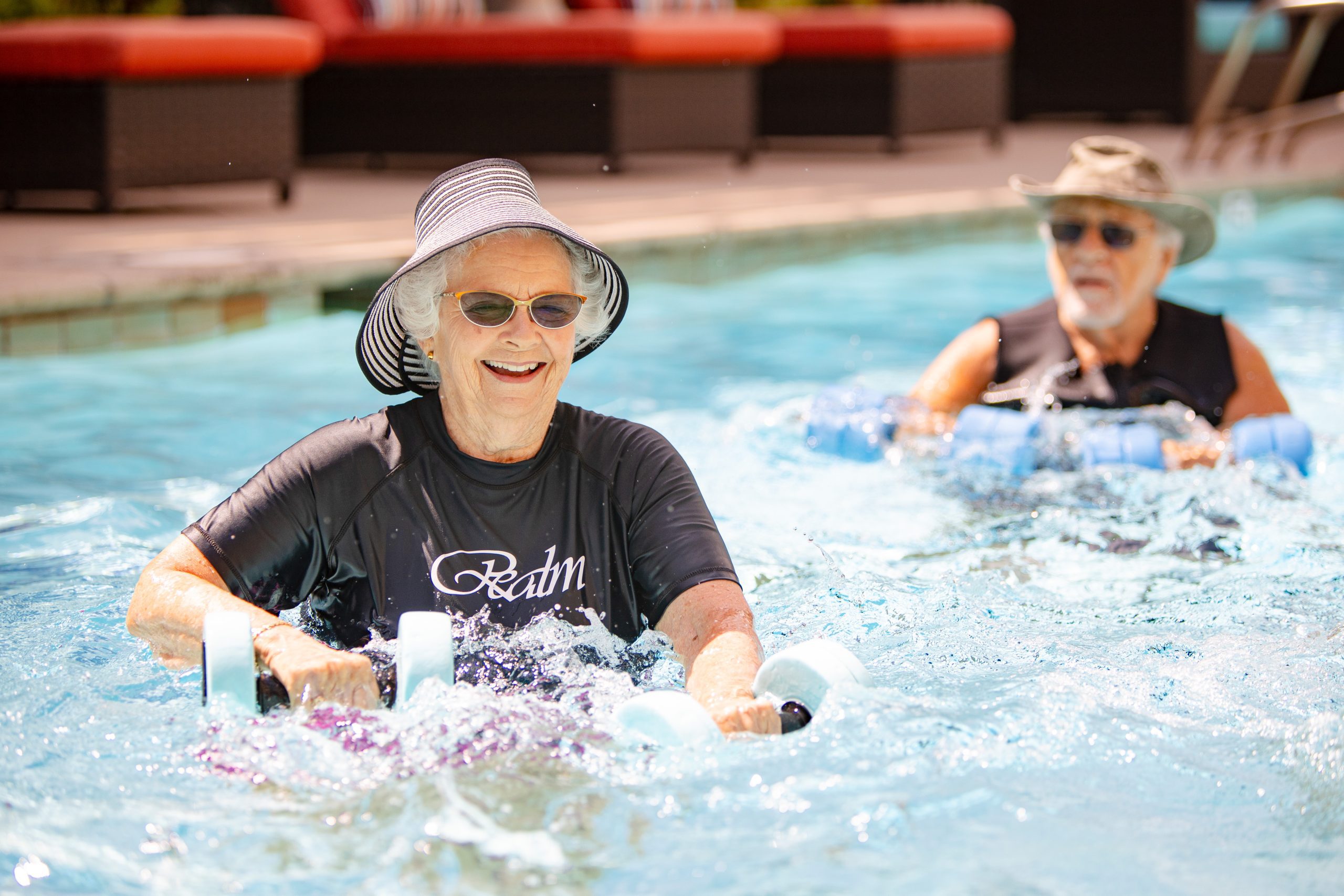 two elderly people doing exercises in the pool with dumbbells