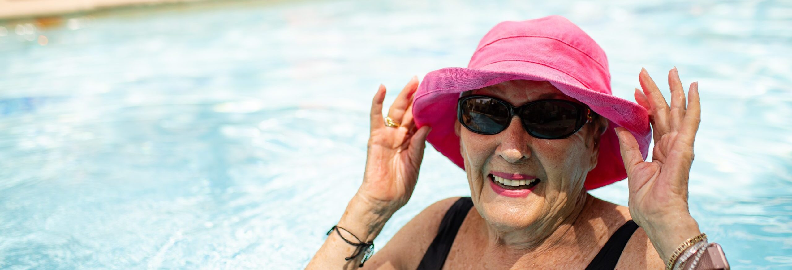 woman swimming in pool with hat and sunglasses smiling