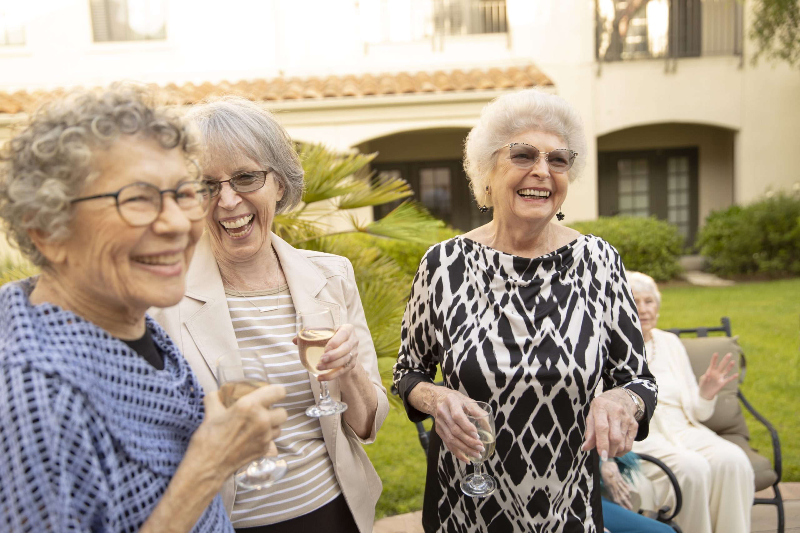 three elderly friends all laughing together while drinking wine