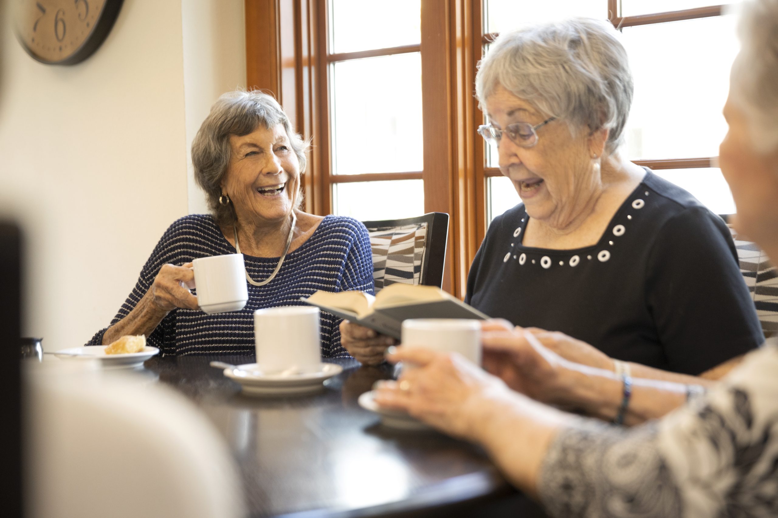 Three elderly women enjoying coffee and reading books together at a table.