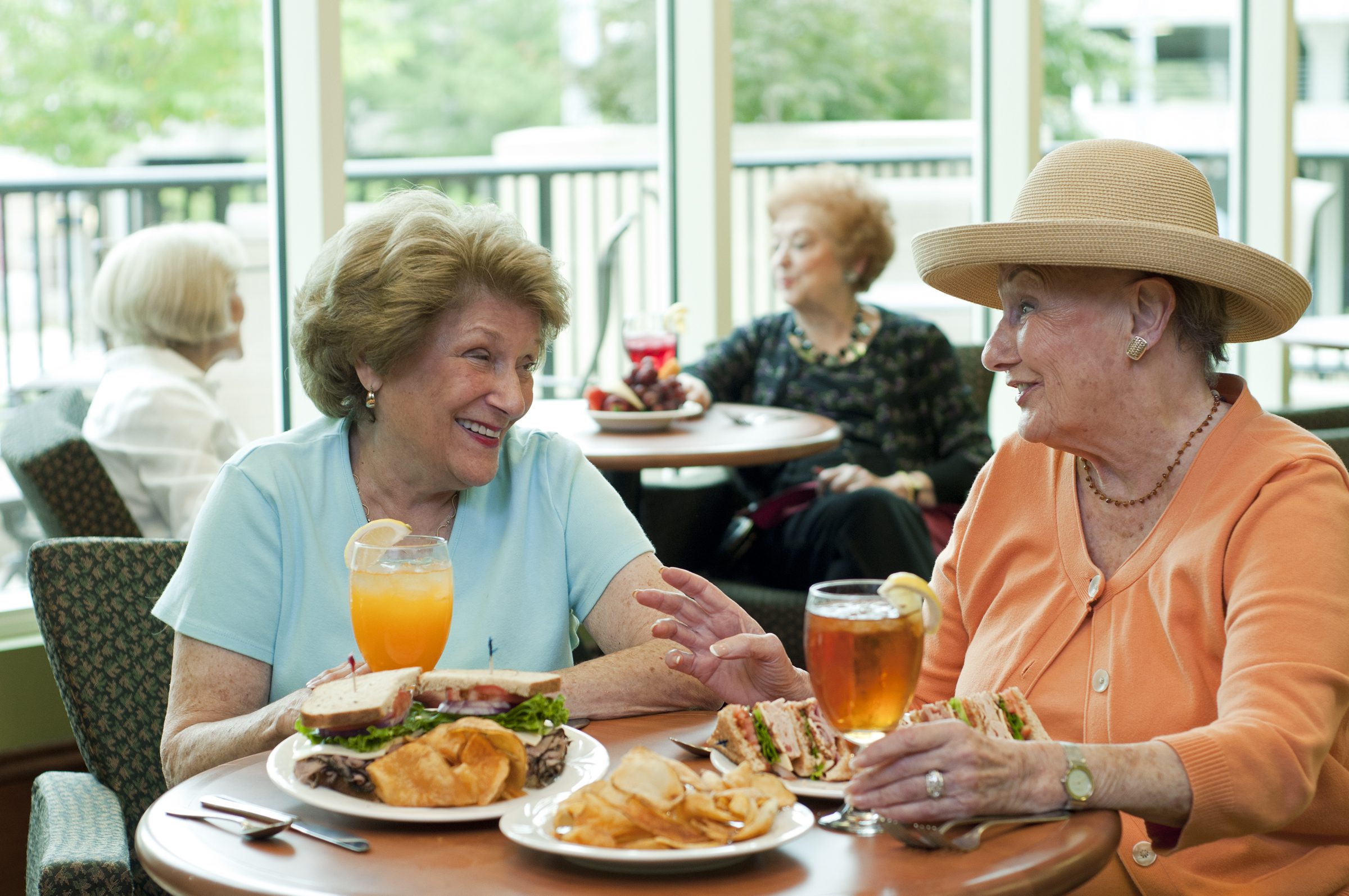 Two elderly women enjoying refreshments and a meal while seated at a table.