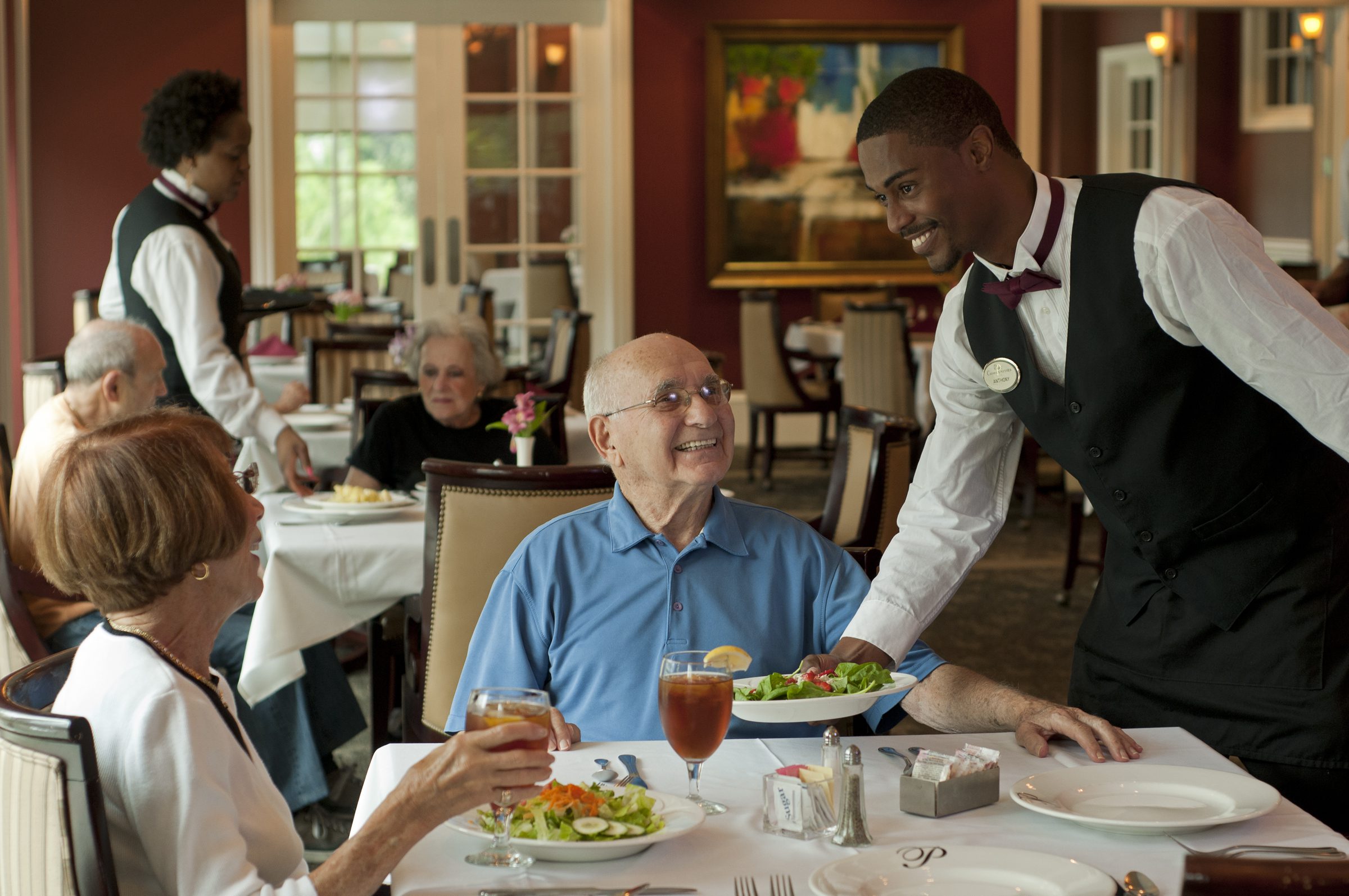 A waiter attentively serves an elderly man at a restaurant, ensuring a pleasant dining experience for the customer.