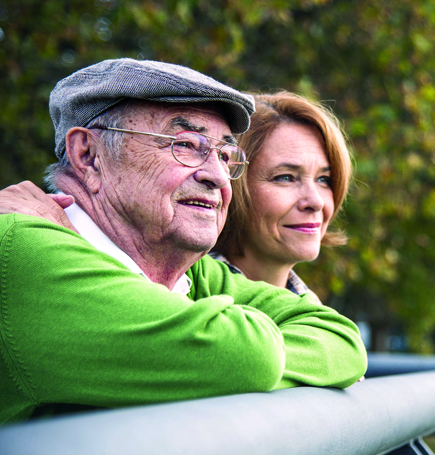 A senior man and his daughter sitting on a bench, smiling and enjoying each other's company in a park.
