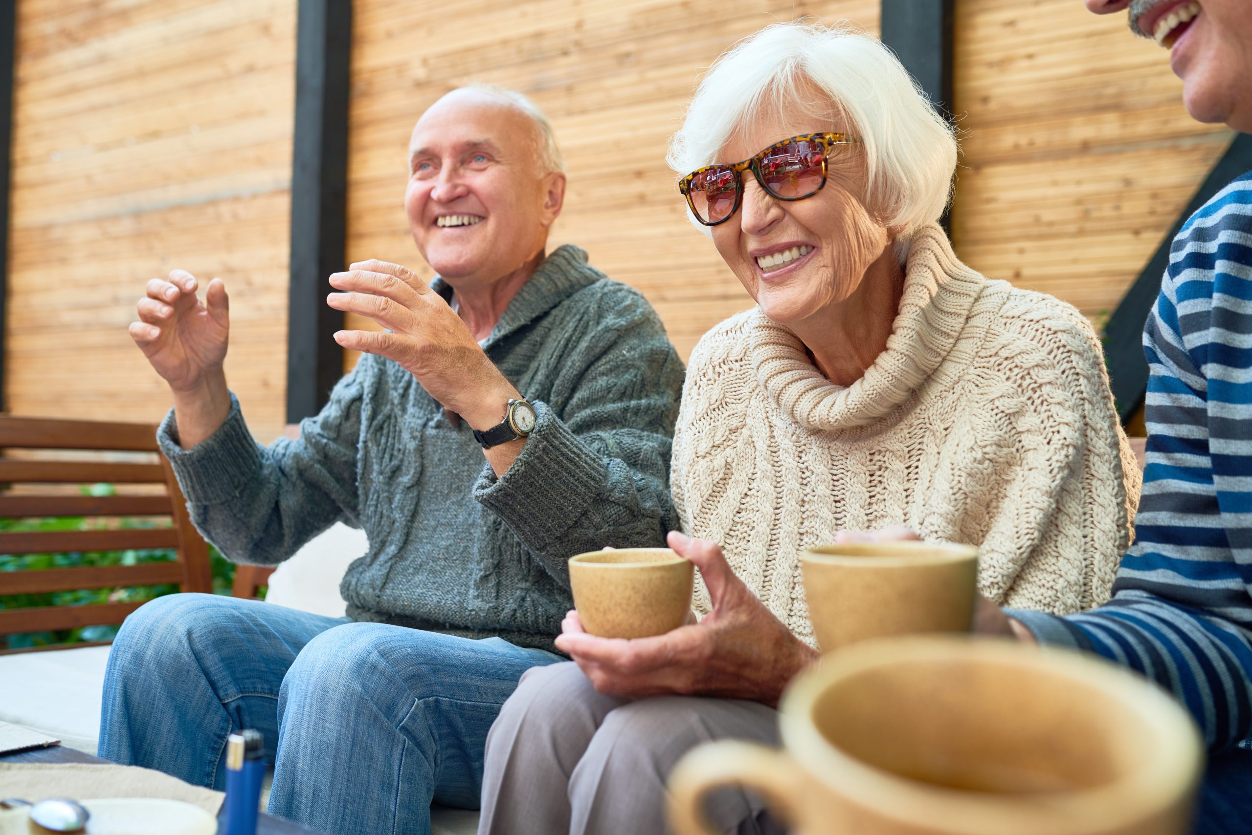 Three seniors enjoying a cozy moment on a couch, sipping coffee from their cups.