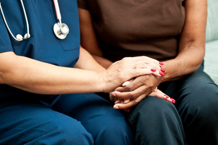 A caring nurse providing comfort to an elderly woman by holding her hand.