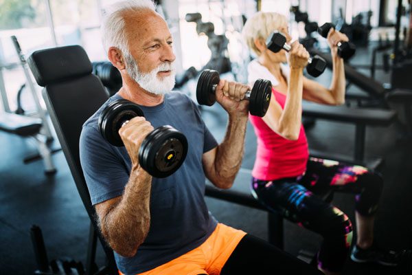 two elderly people doing shoulder presses with dumbbells