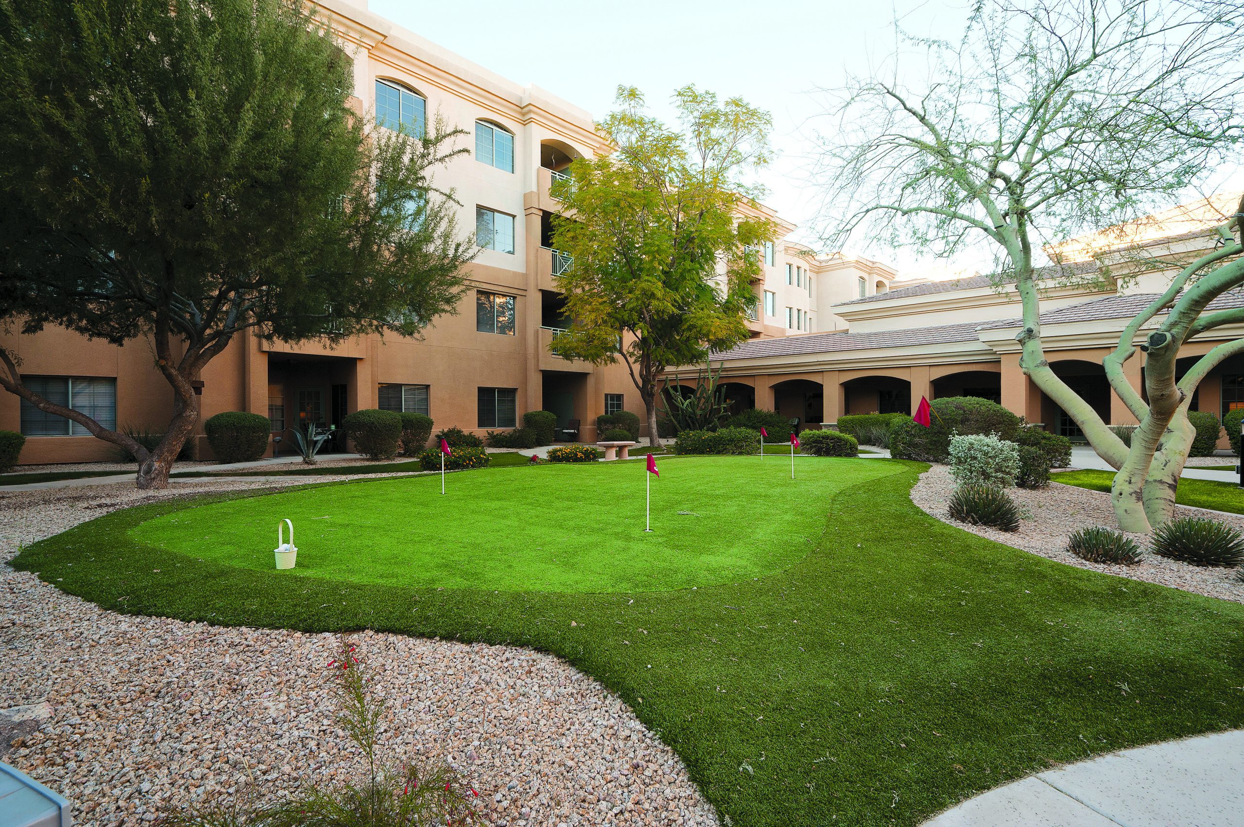 A green putting green in front of a building, providing a serene and inviting space for golf enthusiasts.