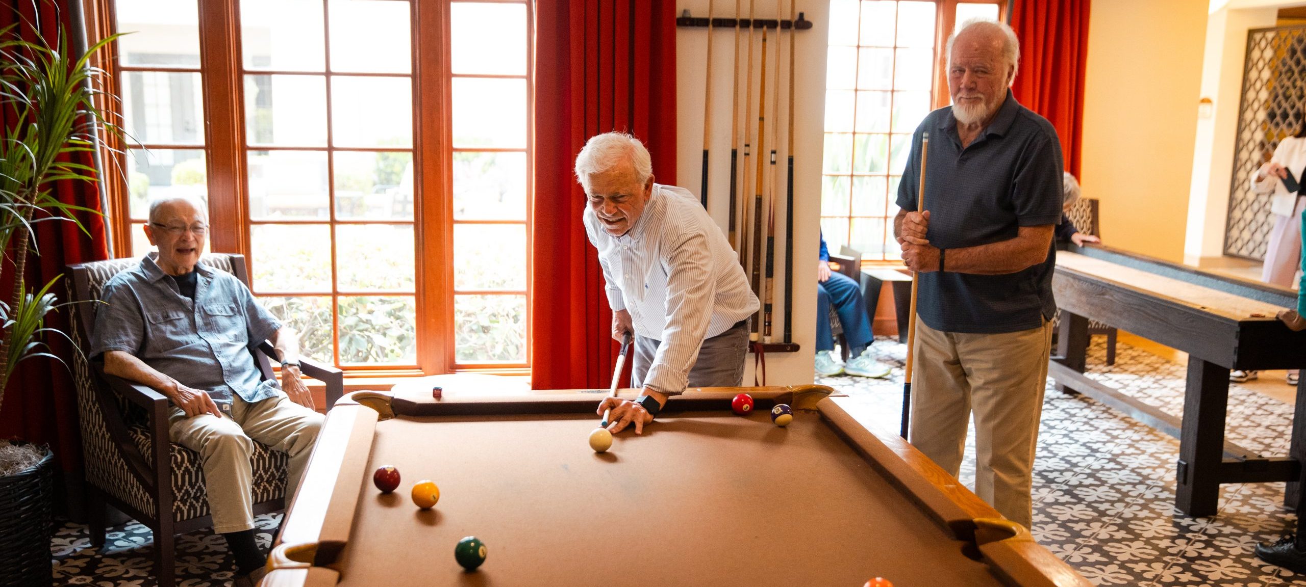 three elderly men playing pool together in game room