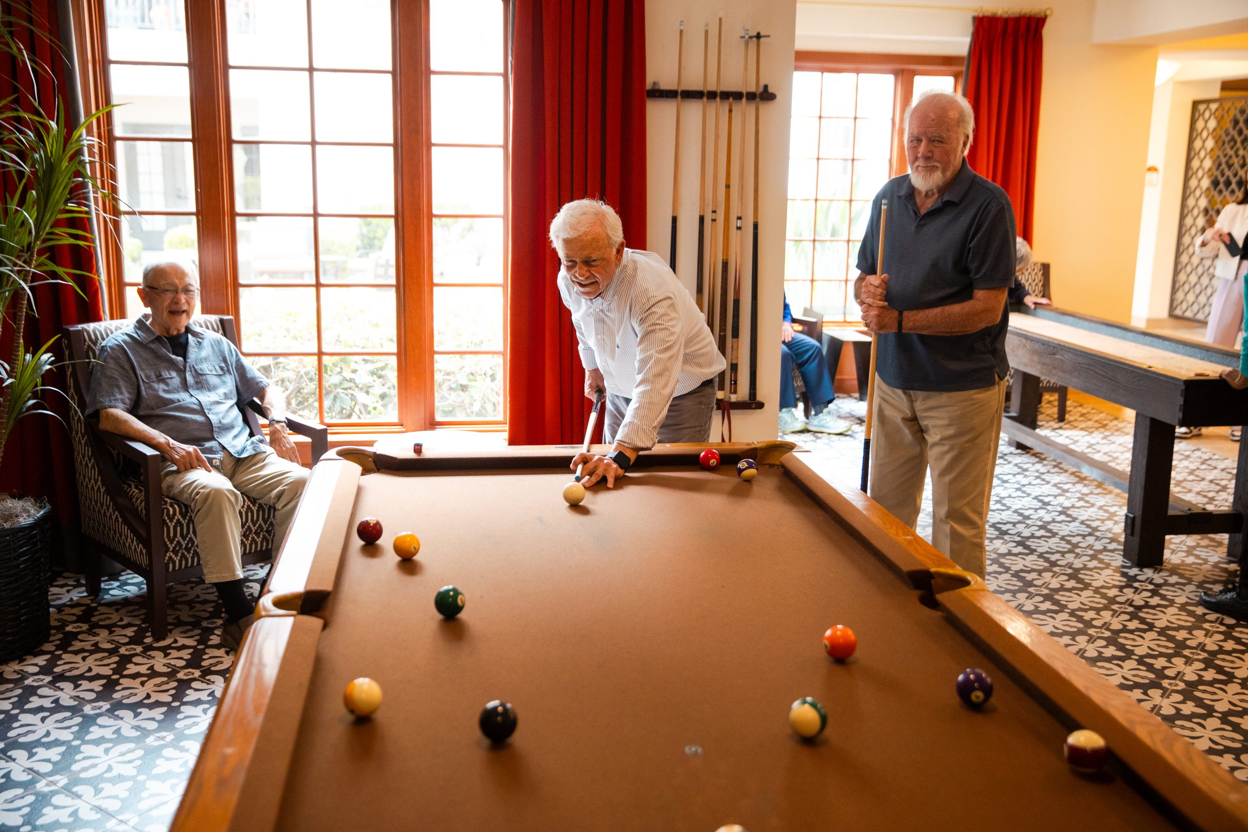 3 elderly men playing pool together in game room