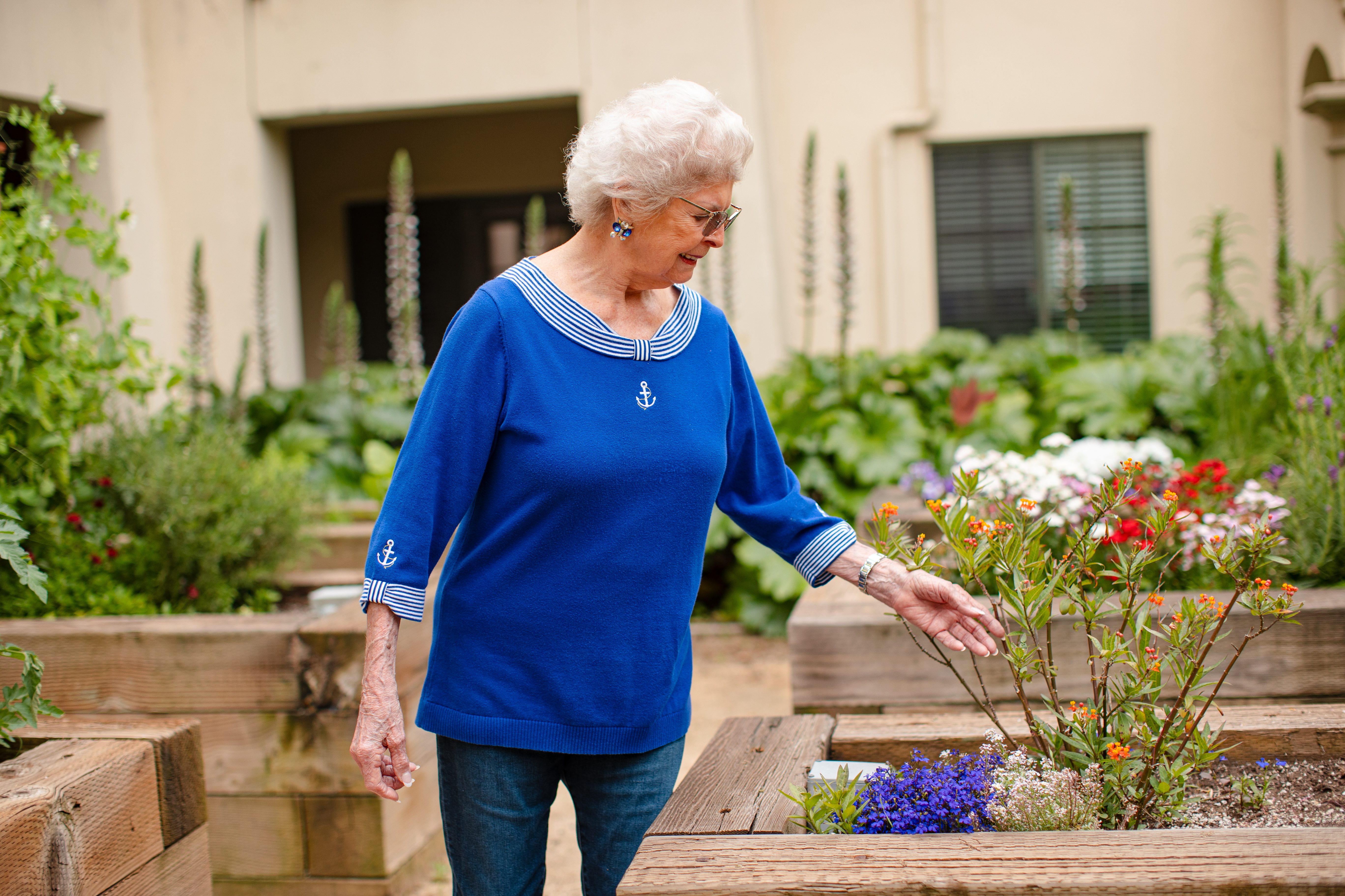 An elderly woman gracefully strolls through a serene garden, wearing a lovely blue dress.