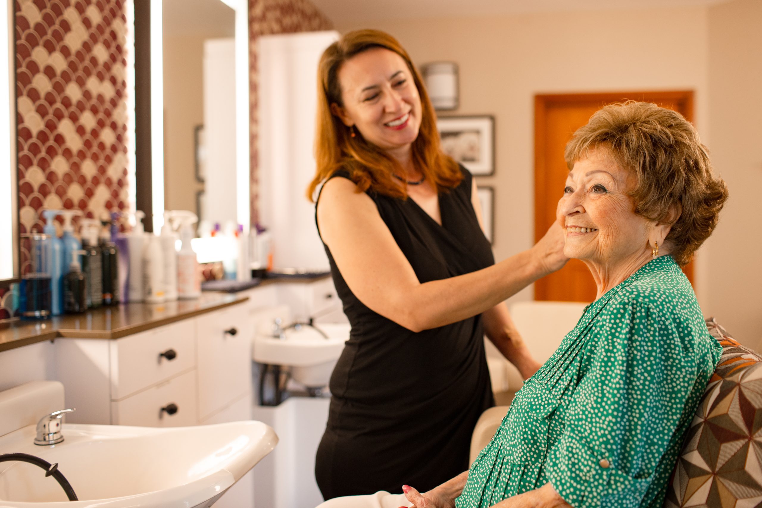 smiling elderly woman getting her hair done at a salon wearing a green shirt