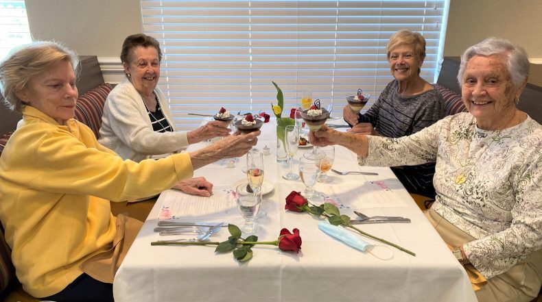 Four women enjoying cupcakes and wine at a table, sharing laughter and conversation.