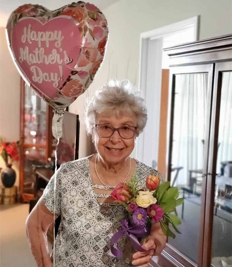 An elderly woman joyfully holds a bouquet of flowers and a heart-shaped balloon, radiating love and happiness.