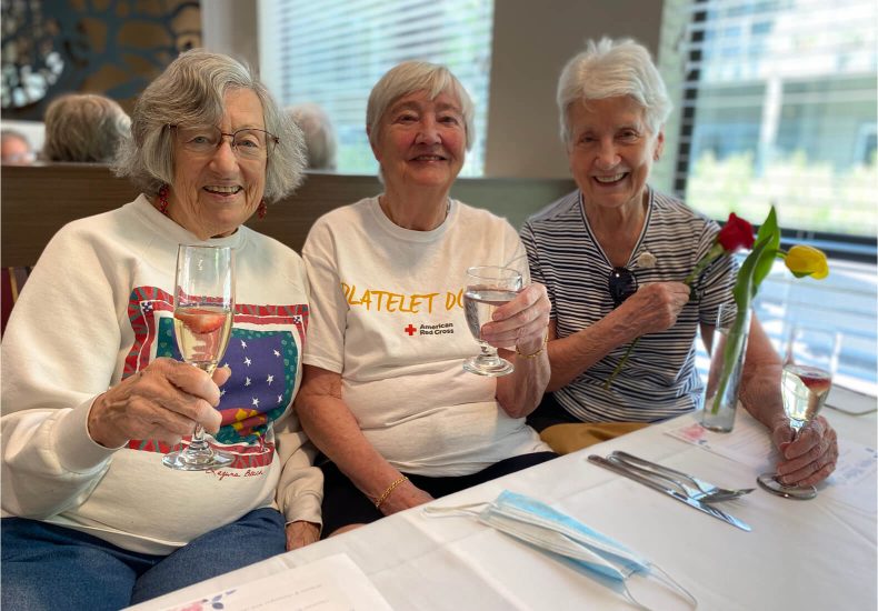 Three older women enjoying a conversation over wine at a table.
