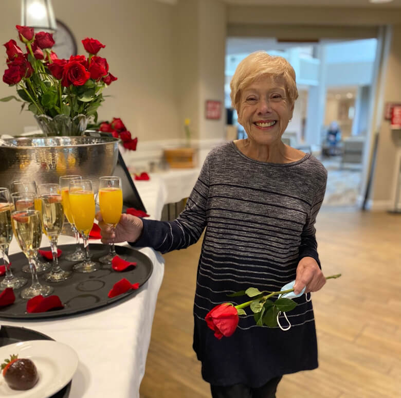 An elegant older woman gracefully holds a rose and champagne, radiating sophistication and charm.
