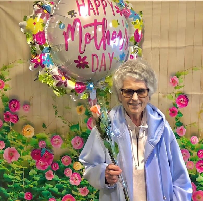 An elderly woman joyfully holds a bouquet of flowers and a balloon with 