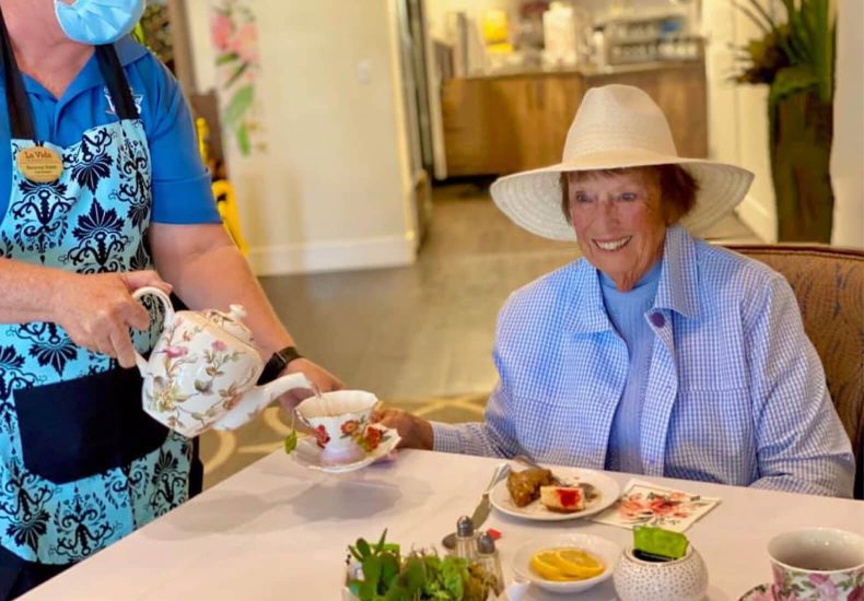 A woman in a hat pouring tea for an elderly woman, creating a warm and comforting atmosphere.