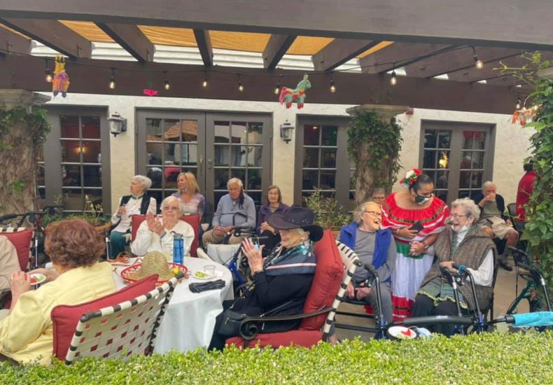 A diverse group of individuals sitting outdoors on chairs, engaged in conversation and enjoying the pleasant weather.