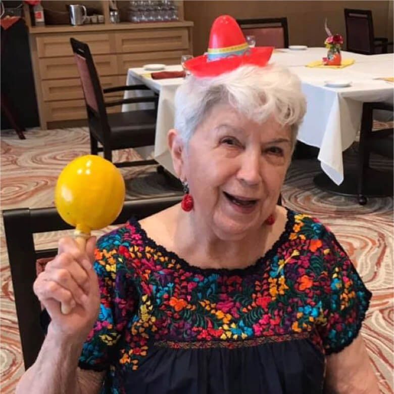 An elderly woman wearing a sombrero, joyfully holding a colorful balloon.