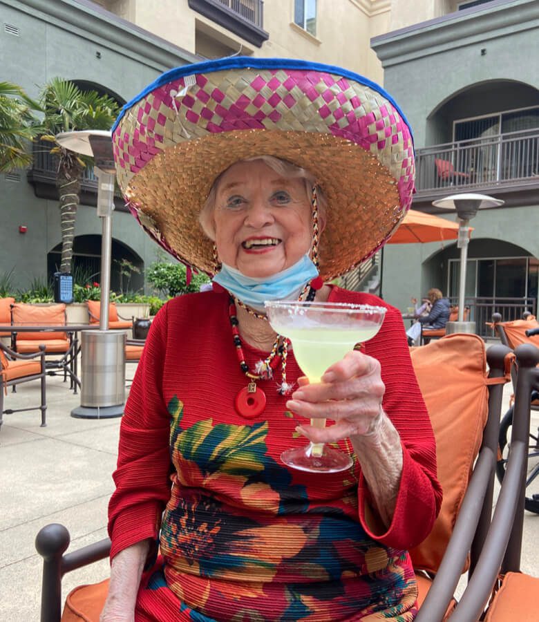 An elderly woman wearing a sombrero, holding a cocktail, and enjoying a leisurely moment.