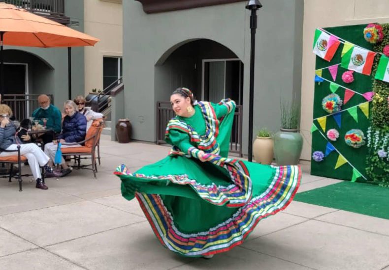 A woman in a vibrant Mexican dress gracefully dances on a sunlit patio, showcasing the rich cultural heritage.