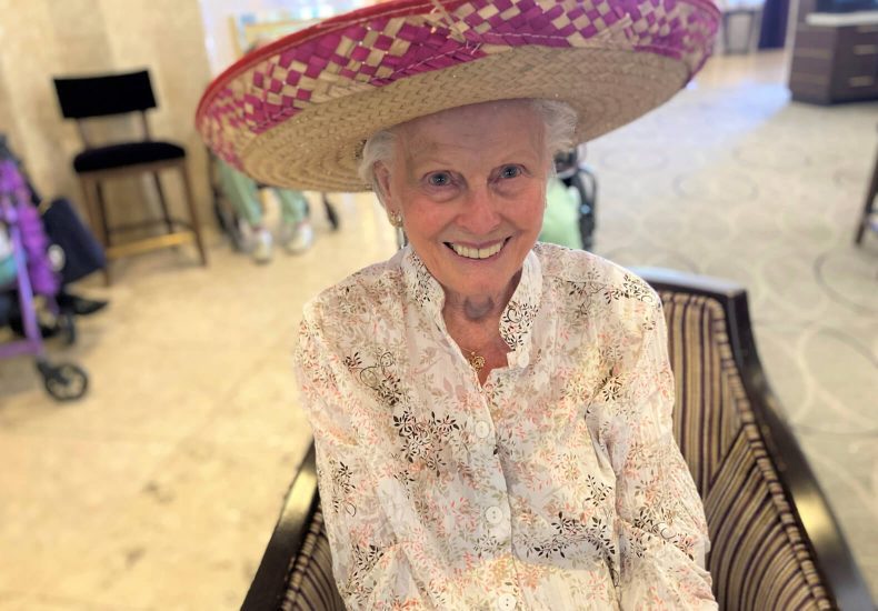 An elderly woman wearing a sombrero sits comfortably in a chair.
