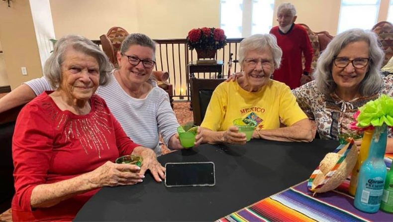 Four older women enjoying drinks at a table, engaged in conversation and sharing laughter.