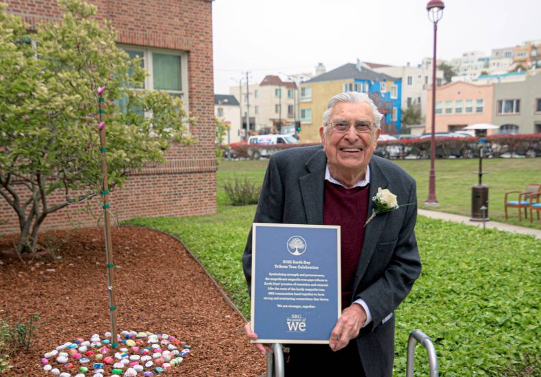 An elderly man proudly displaying a plaque in front of a majestic building