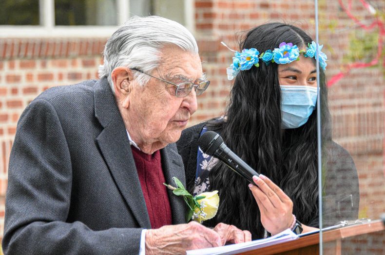An elderly man wearing a face mask and a woman wearing a flower crown, standing together.