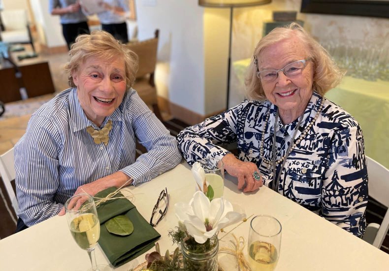 Two elderly women enjoying a conversation over wine at a table.
