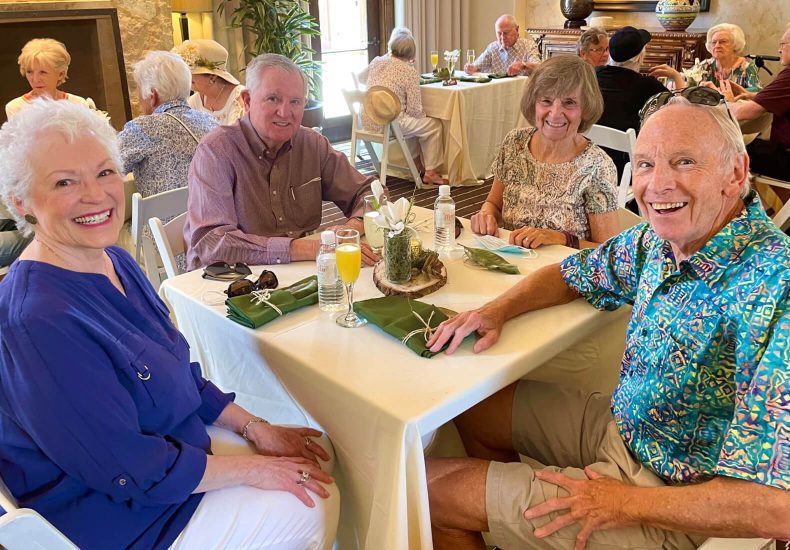 A joyful gathering of elderly individuals seated around a table, wearing smiles on their faces.