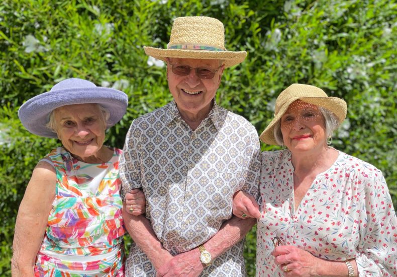 Three elderly individuals wearing hats, standing closely together, smiling and posing for a photo.
