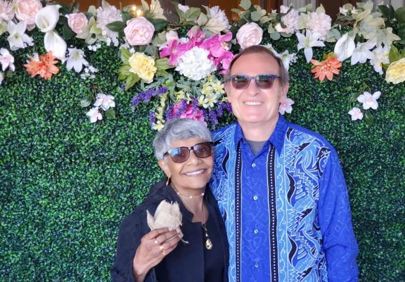 A couple posing in front of a beautiful floral wall, creating a vibrant and romantic backdrop.