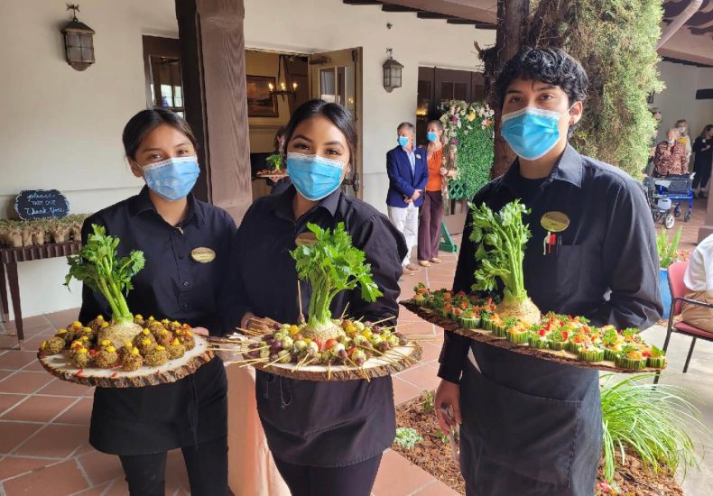 Three people in face masks holding trays of food.