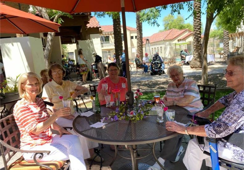 Four women enjoying a meal at an outdoor table, sheltered by colorful umbrellas.