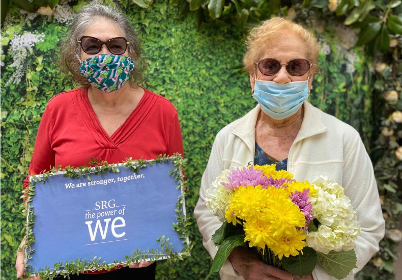 Two women wearing masks and holding flowers, symbolizing unity and hope during challenging times.