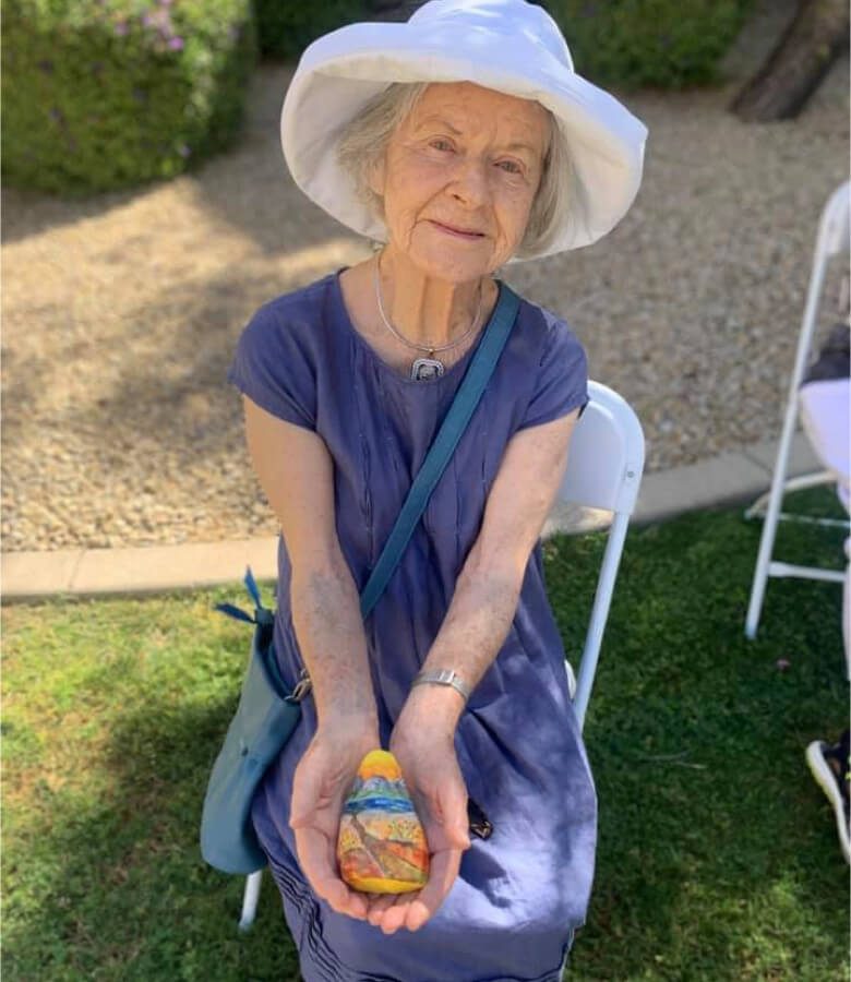 An elderly woman wearing a hat gently cradles a tiny egg in her hands.