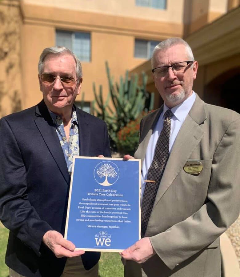 Two men in suits holding a plaque outside, possibly during a formal event or ceremony.