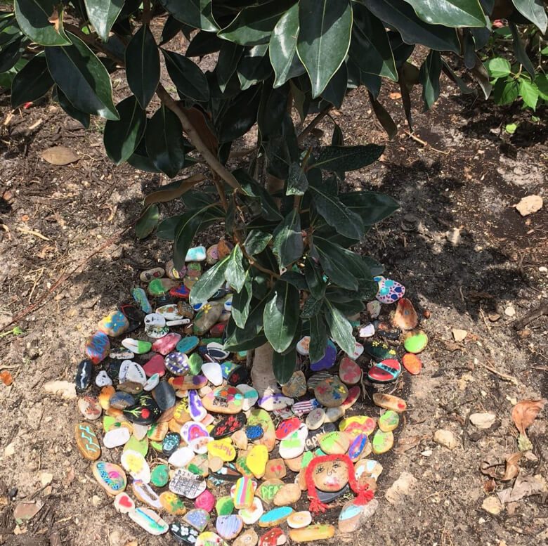 A vibrant tree surrounded by a multitude of colorful rocks scattered on the ground.