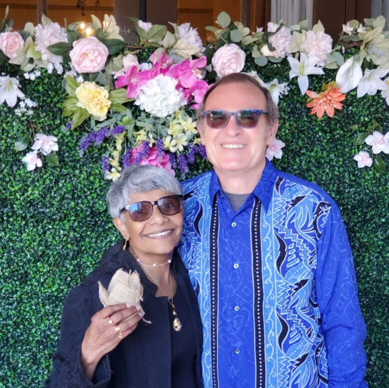 A couple posing in front of a beautiful floral wall, creating a vibrant and romantic backdrop.