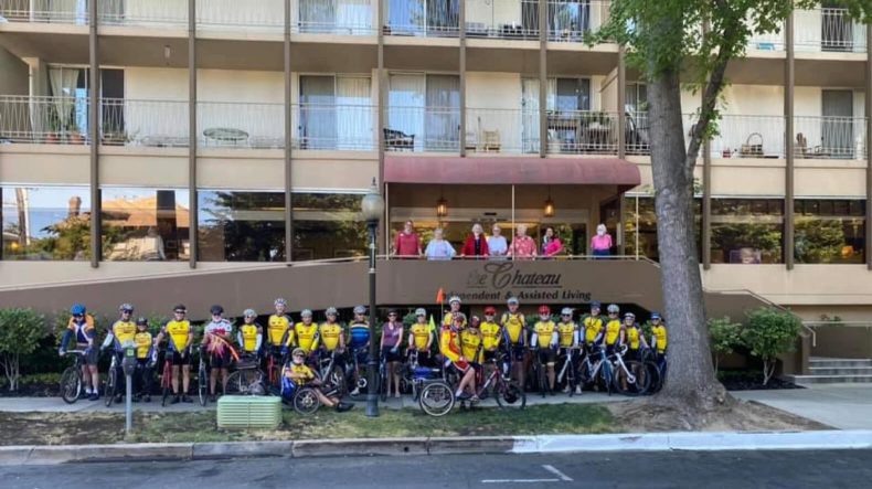 A group of people in yellow shirts and bikes standing in front of a building.