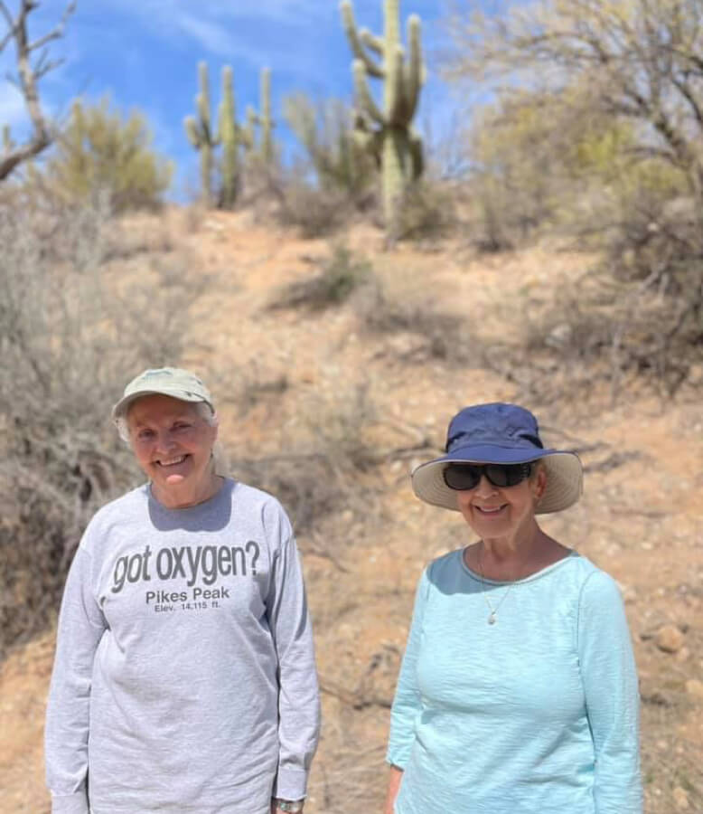 Two women posing in front of a tall cactus, showcasing the beauty of nature and friendship.