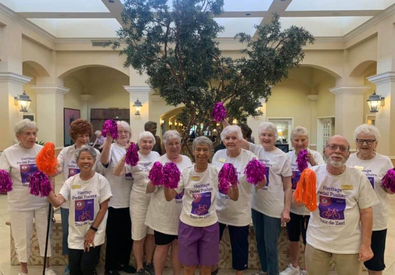 A group of elderly individuals wearing white shirts and holding purple pom poms.