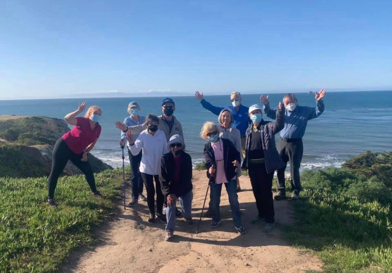 A group of people standing on a trail near the ocean, enjoying the scenic view and the refreshing sea breeze.