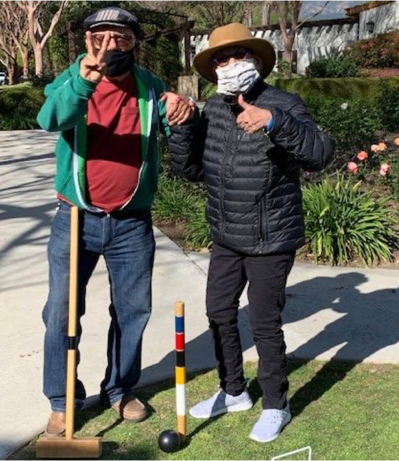 Two individuals wearing face masks, holding croquet sticks.