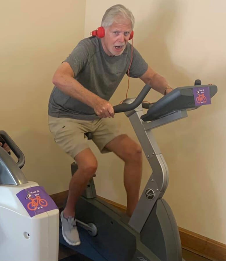 An elderly man wearing headphones while cycling on an exercise bike.